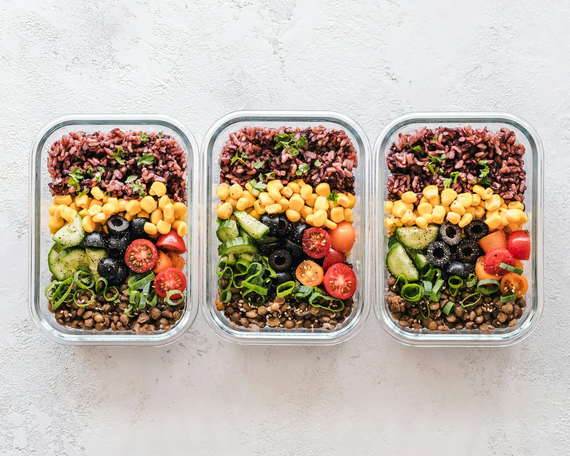 Three meal prep containers with grains and vegetables